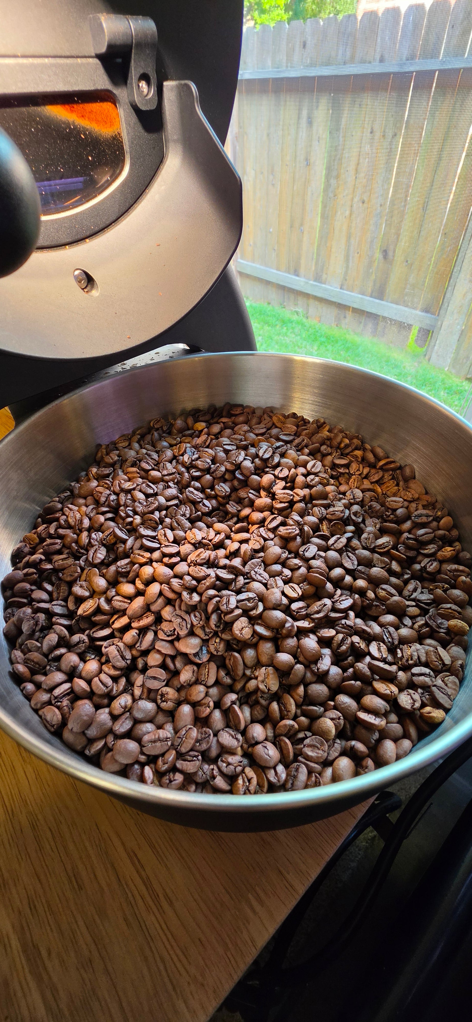 Metal bowl filled with coffee beans next to a coffee grinder outdoors.